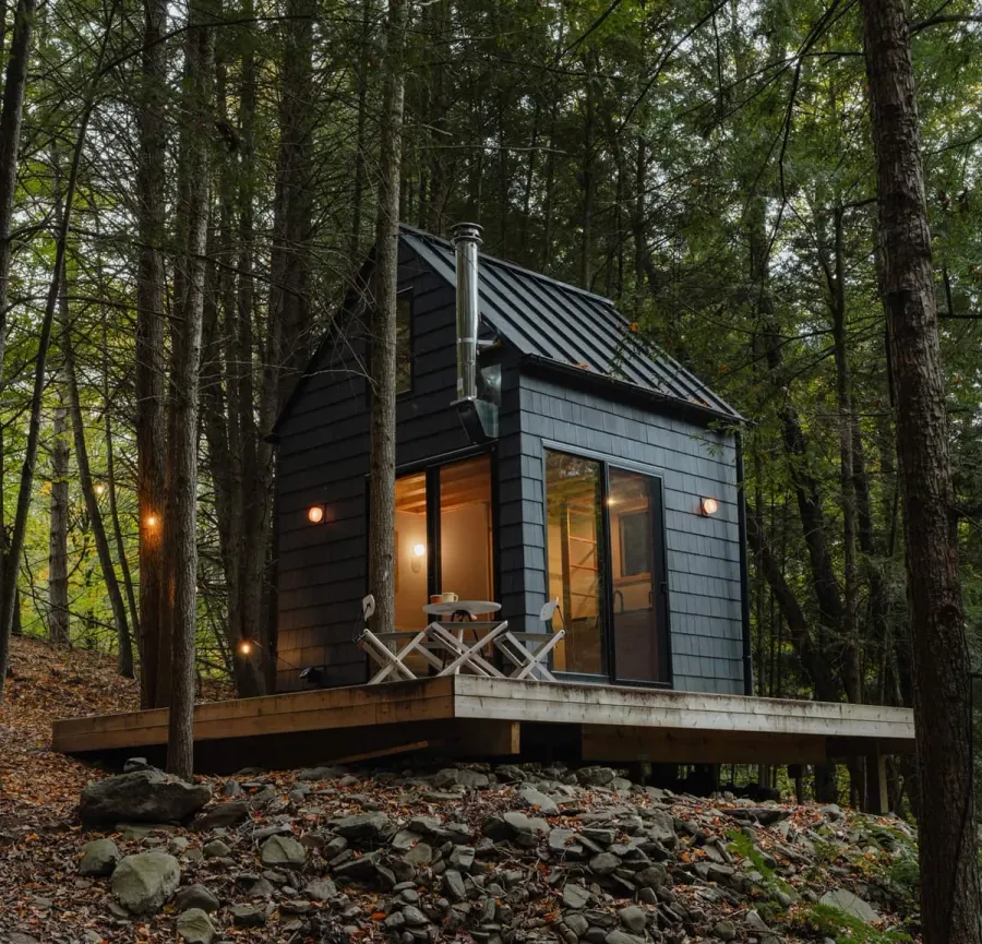 A dark HUTS cabin at night, its tall windows glowing, on a deck among the trees.